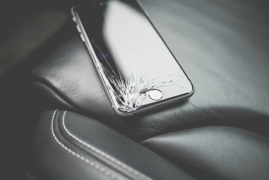 Black iPhone 6 with cracked screen on a black car seat.