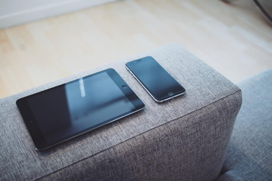 A black iPhone and iPad on the armrest of a couch.