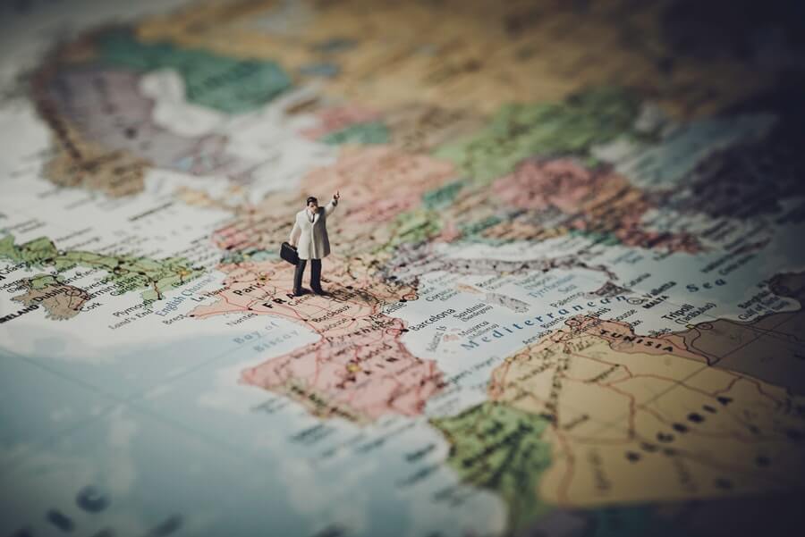 Tiny business person figurine on a map of Europe, standing on France and hailing something.