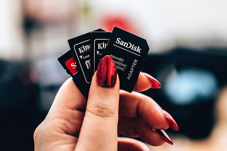 Woman's hand with interesting red fingernails holding SD cards and microSD card adapters from SanDisk and Kingston.