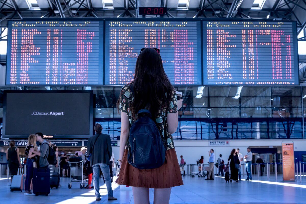 Girl standing in front of flight information display at airport arrivals and departures terminal.