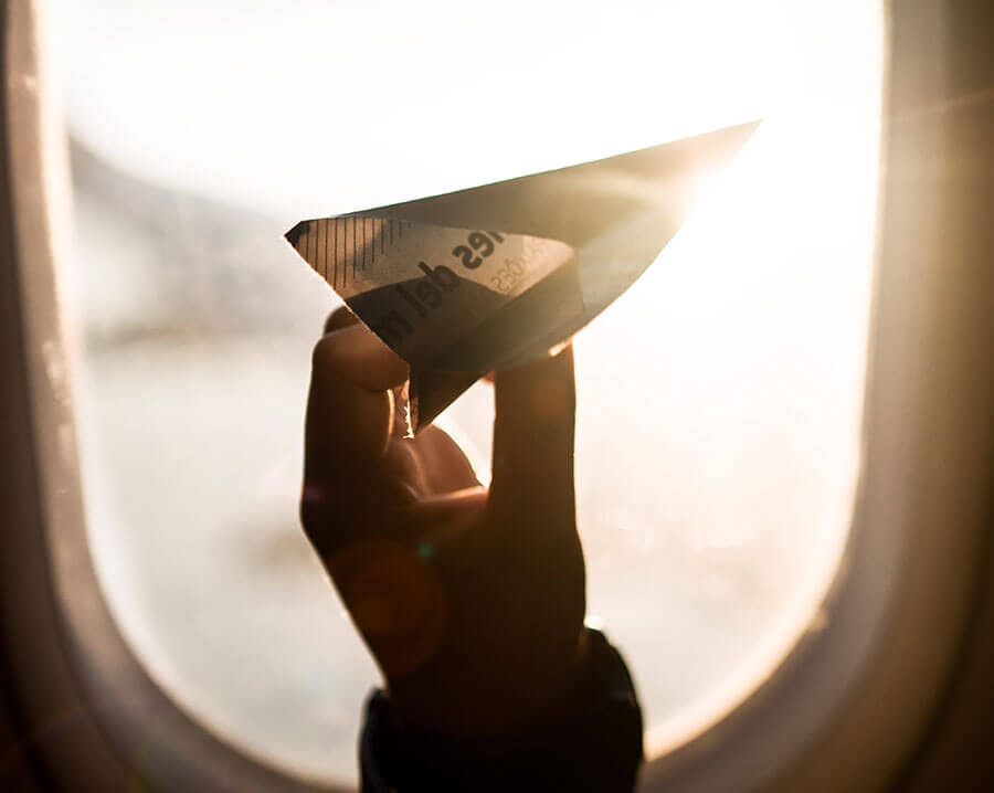 Hand holding paper airplane inside real airplane.