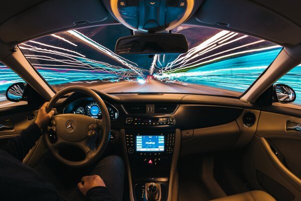 Interior view of driver in Mercedes Benz driving down the street at night with blurred city lights around the car.