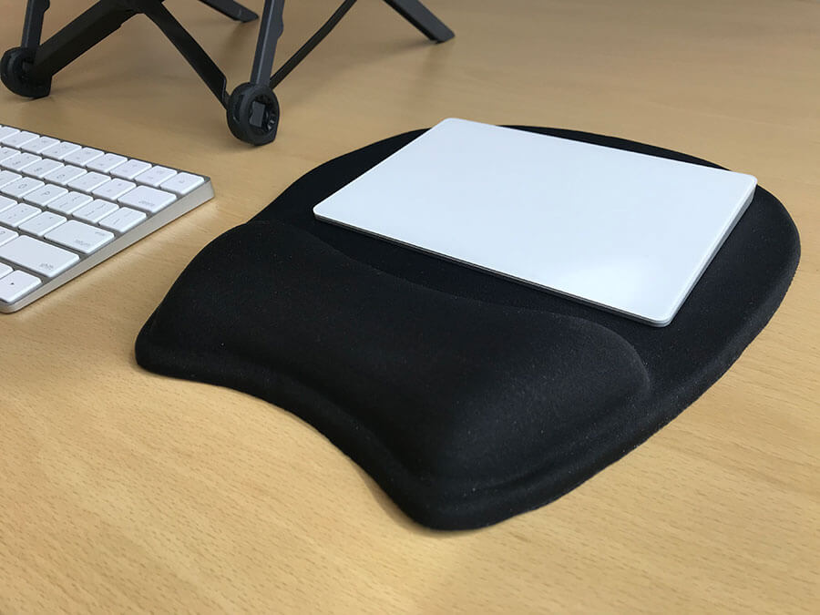 Apple Magic Trackpad 2 resting on a mousepad (with wrist rest), with an Apple Magic Keyboard 2 and Roost Laptop Stand in the background.