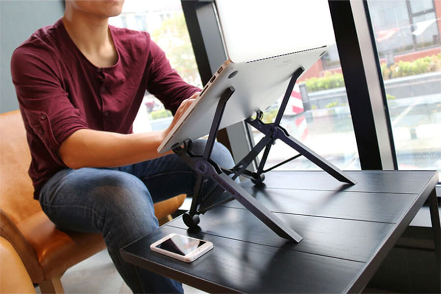 Man using Nexstand K2 (laptop stand) awkwardly in cafe without keyboard or mouse/trackpad.