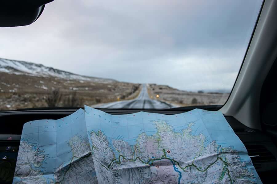 Map with route drawn on it resting on the dashboard of a car on a road trip through the countryside on a dark day.