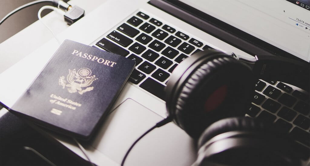 Pair of over ear headphones and passport on laptop on folding tray in airplane.