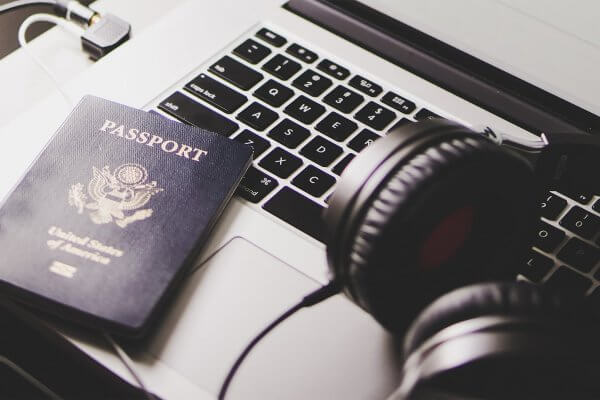 Pair of over ear headphones and passport on laptop on folding tray in airplane.