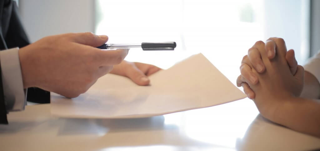 Offering a pen to sign a contract to someone who is pensative with closed hands.
